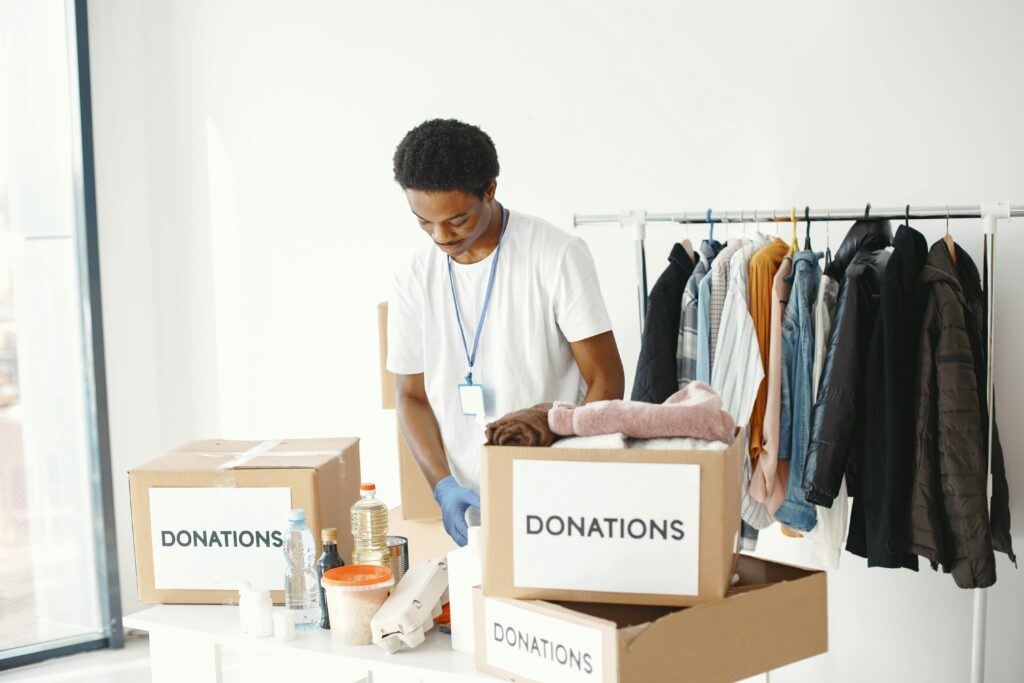 A volunteer organizes donations in a community center, featuring boxes labeled "Donations" and a clothing rack.